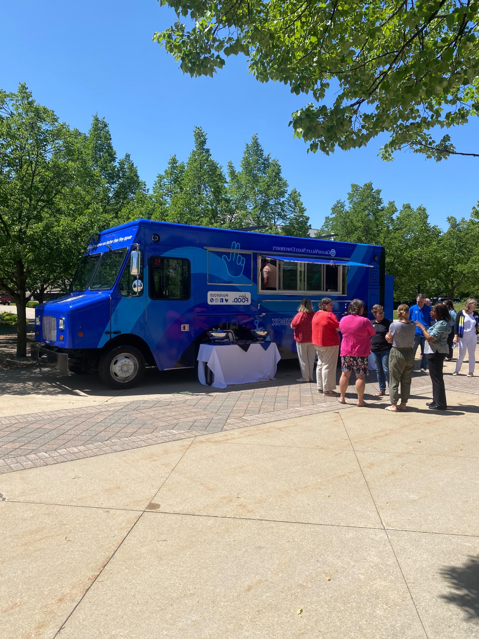 group of people standing next to Louie's Lunchbox food truck on GVSU's campus